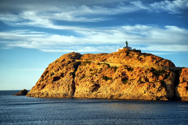 Le phare de la Pietra et ses rochers éclairés par le soleil couchant.