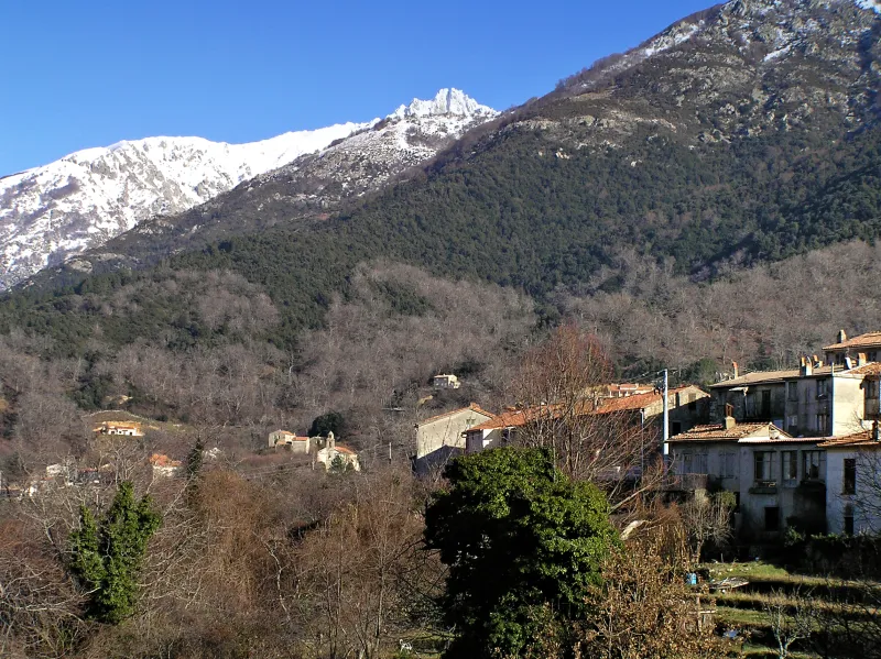 Maisons de Bocognano sous les versants boisés et les sommets enneigés.